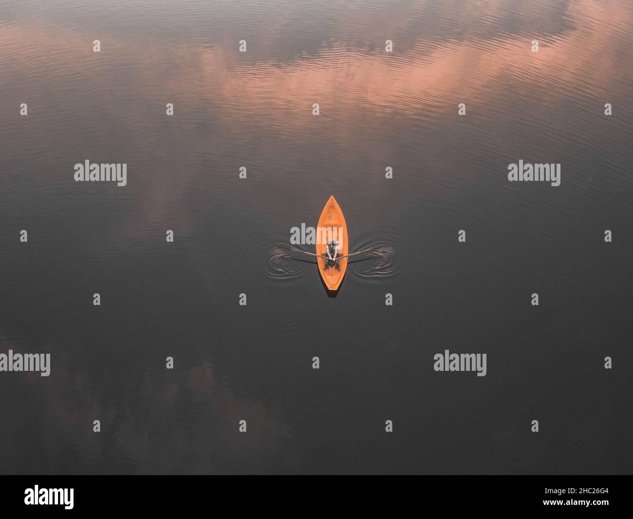 Aerial shot of man rowing a boat. Clouds reflecting on lake surface ...