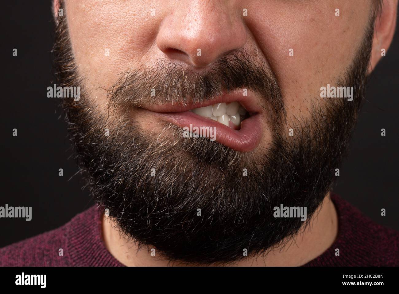 rage, fury grin, closeup on face and lips of young unrecognizable man with black beard and mustache, baring his teeth Stock Photo