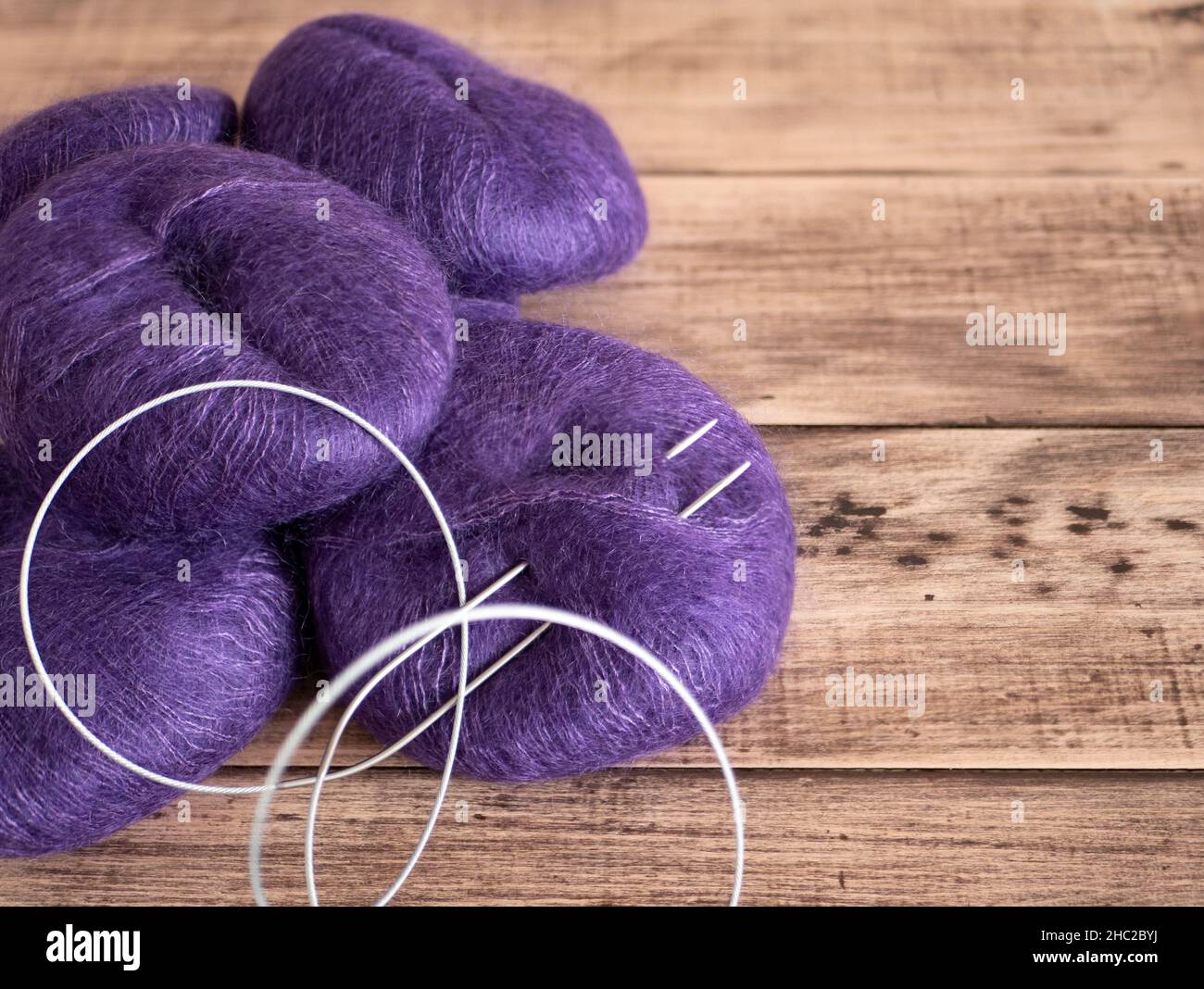Purple yarn and needles for knitting, close up. Balls of thread and fixed circular knitting needles on rustic wooden background Stock Photo