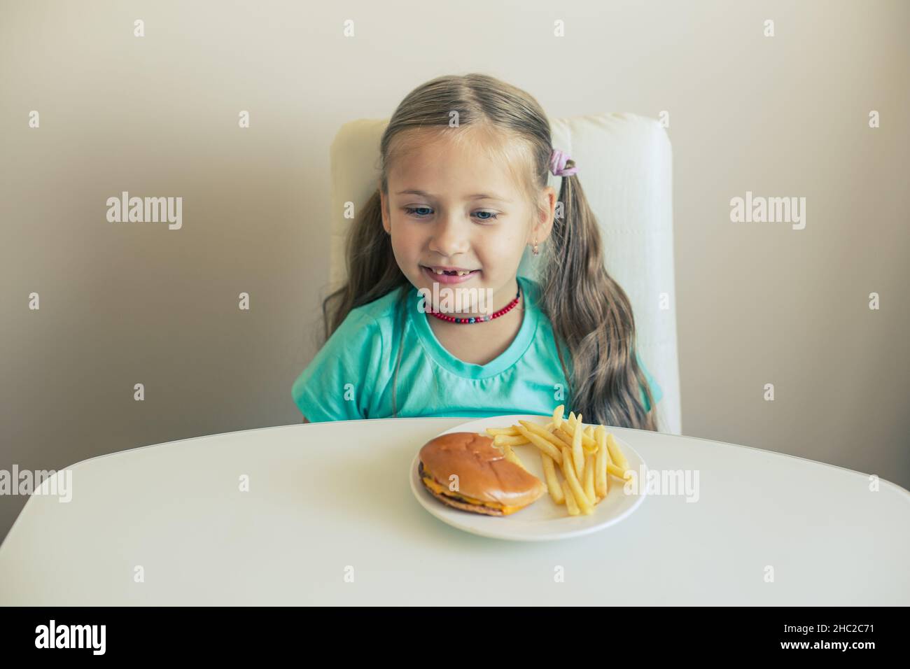 Smiling Little girl seats by the table with hamburger and French fries dish Stock Photo