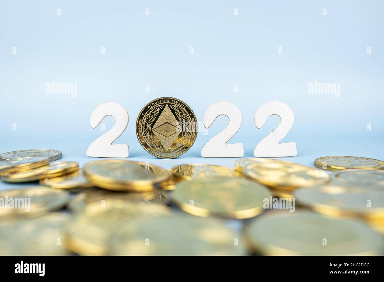 Ethereum 2022 price prediction concept. Ether coin standing next to cryptocurrency tokens and year numbers on blue background. Close-up, soft focus. Stock Photo