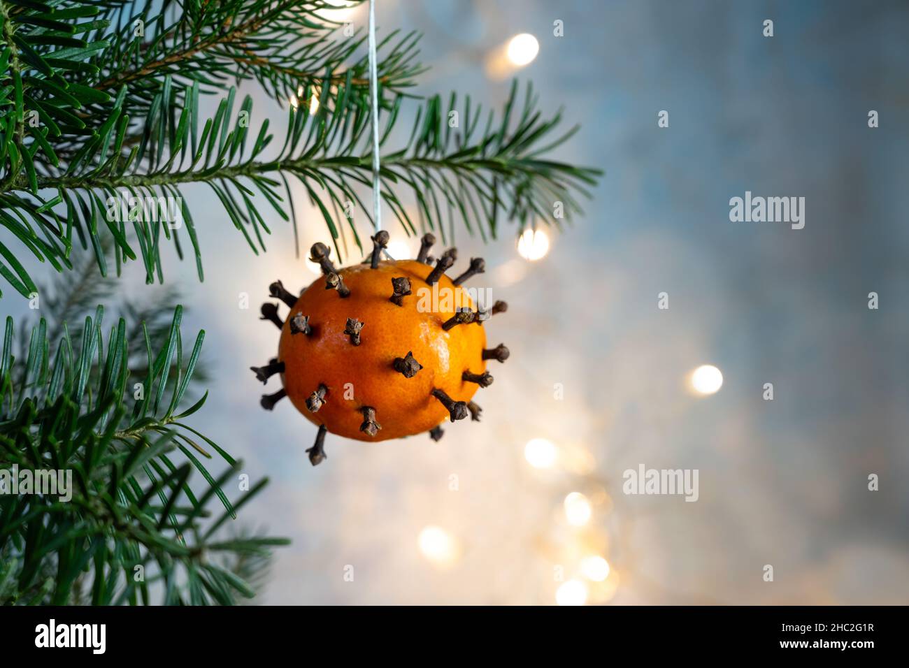 Christmas with SARS-CoV-2 Omicron variant, tangerine spiked with cloves as decoration and covid-19 symbol on the fir tree, background with bokeh light Stock Photo