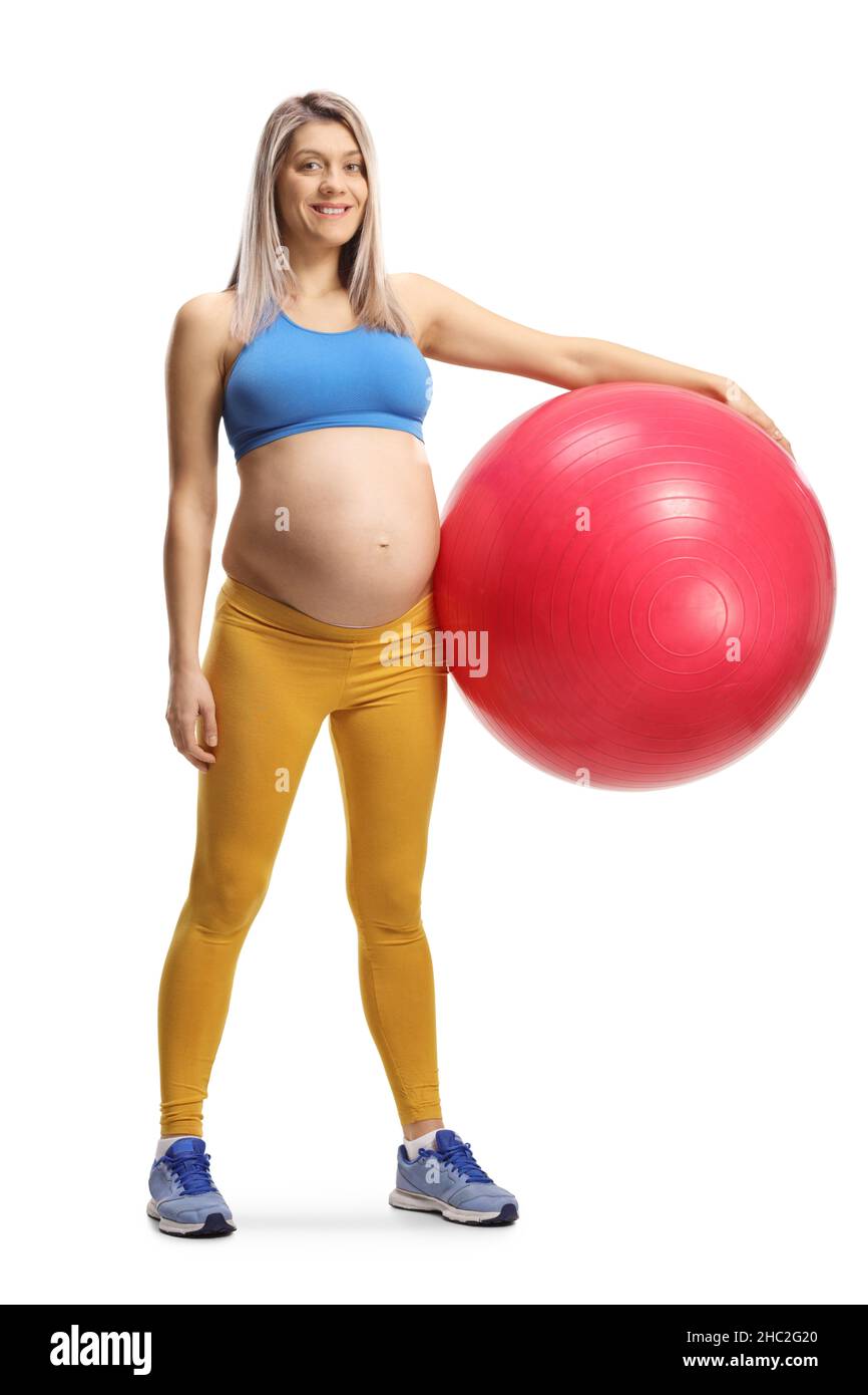 Full length portrait of a pregnant woman with a crop top and leggings holding a fitness ball isolated on white background Stock Photo