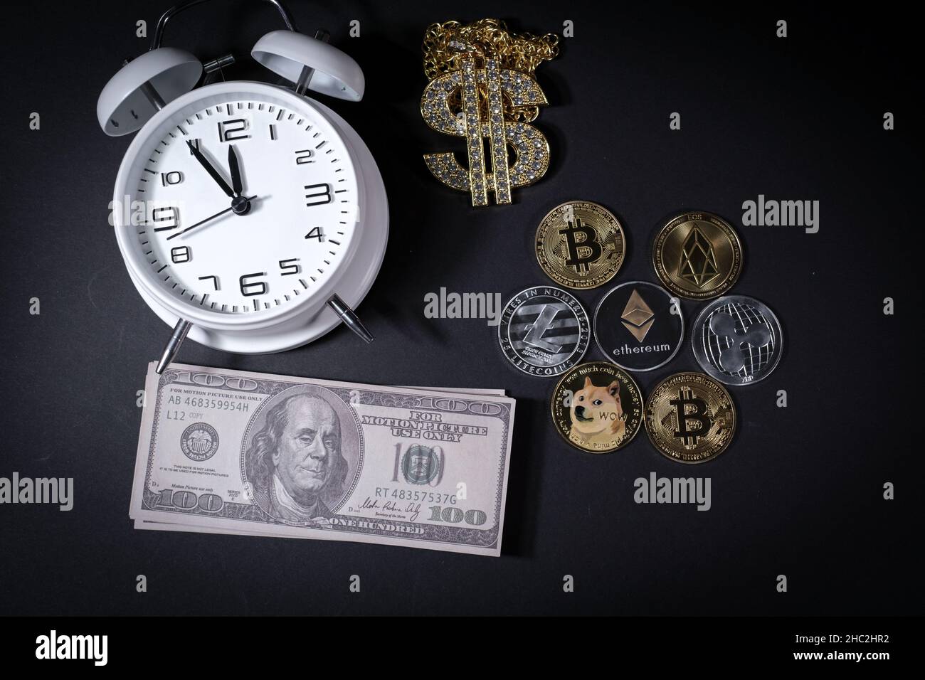 some various crypto coins lie next to a stack of 100-dollar bills, a white  alarm clock and a diamond-studded dollar chain pendant Stock Photo - Alamy