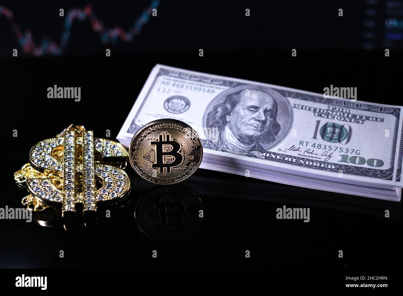 two Bitcoin coins lie next to a stack of $100 bills and a diamond-studded  dollar chain pendant Stock Photo - Alamy