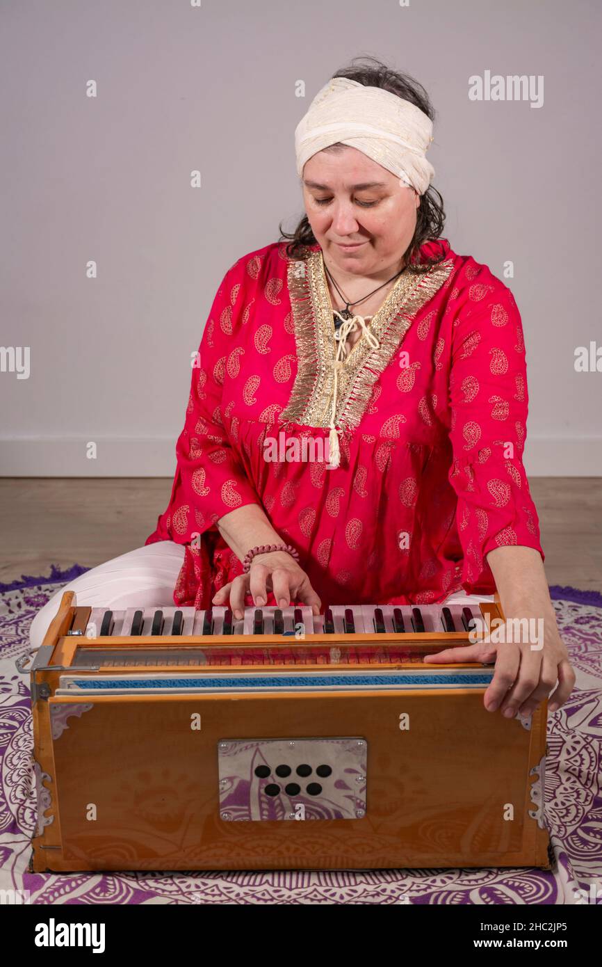 Woman in traditional red dress and turban sitting on the floor playing the harmonium in a kundalini yoga practice Stock Photo