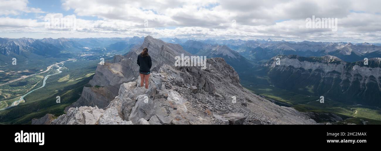 Wide panoramic shot of female hiker enjoying the views on valley from mountain summit Stock Photo