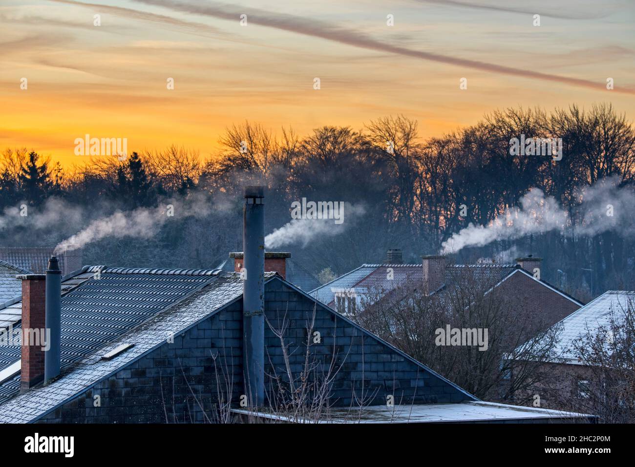 Smoking domestic rooftop chimneys from houses emitting vapour / vapor from gas boilers for central heating at sunrise on freezing cold winter morning Stock Photo