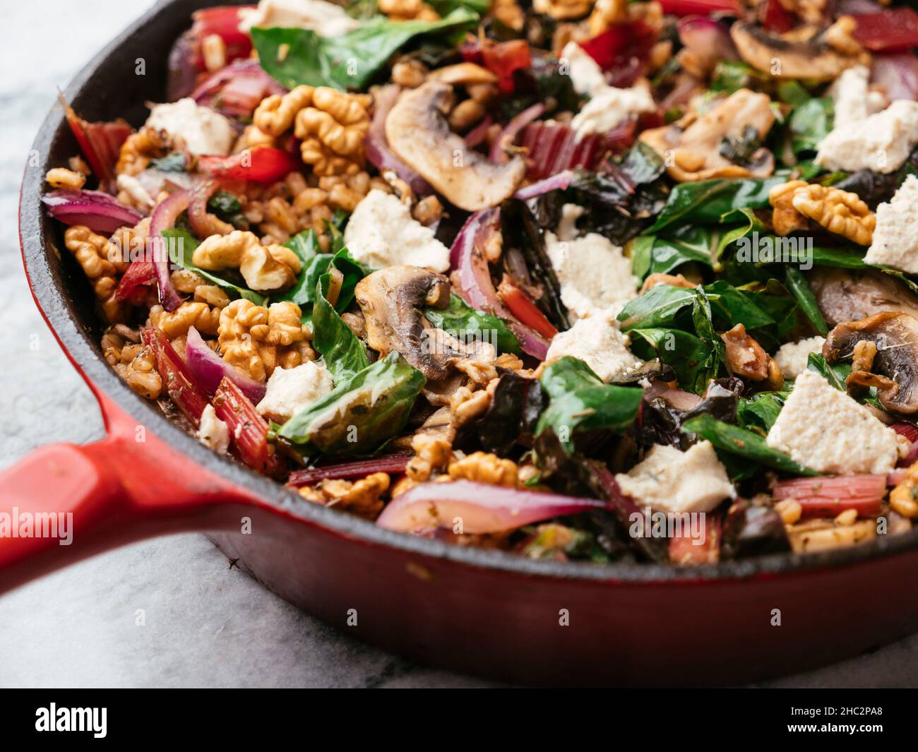 Spelt with red swiss chard, mushrooms, walnuts and vegan feta in a cast iron pan. Stock Photo