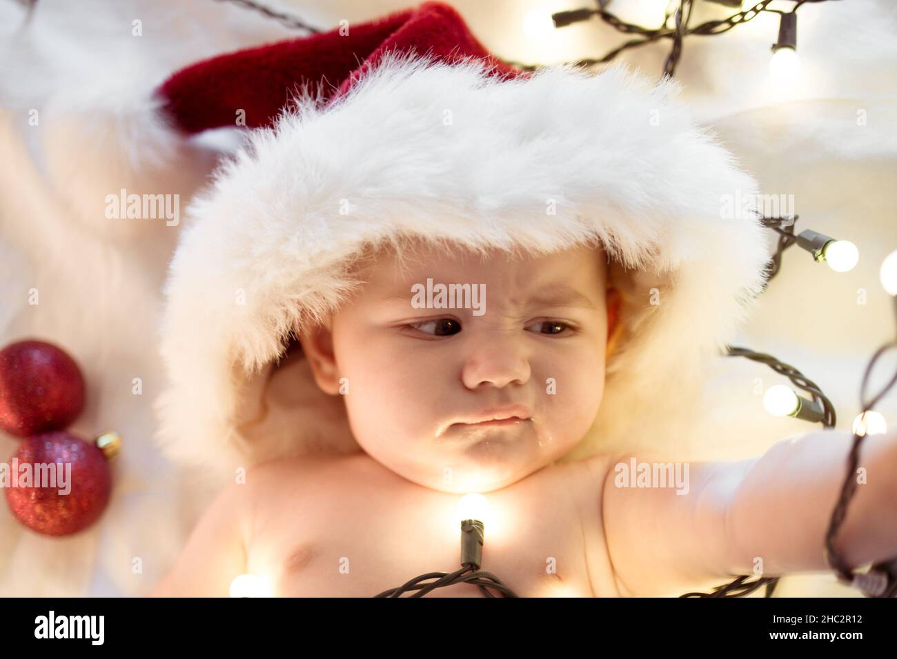 baby with funny look on face, christmas lights, red ornaments Stock Photo