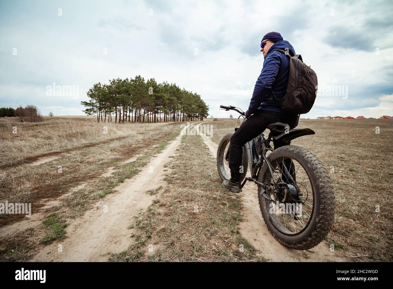 A man on a bicycle with thick wheels and an electric motor. Rural area. Stock Photo