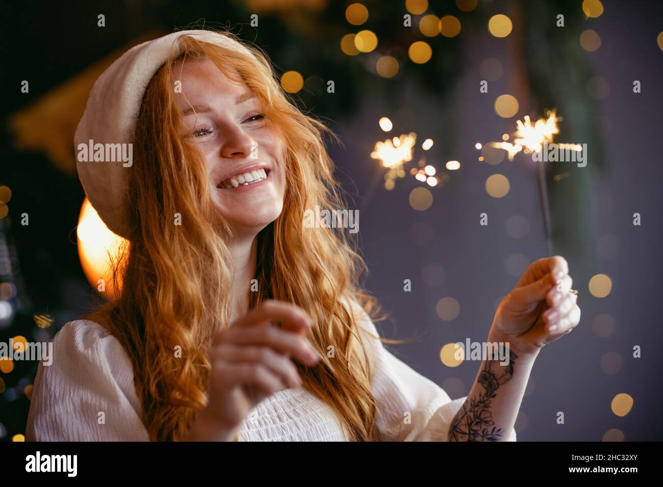 charming red-haired girl in a santa hat with sparklers in her hands smiling at the camera. Stock Photo