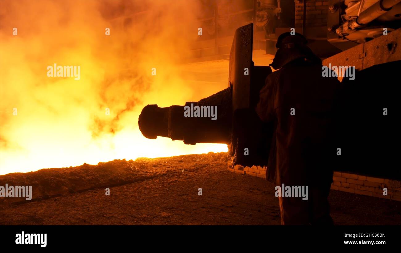 Steel worker near the molten metal flowing in the chute. Metallurgical equipment and technology of iron production. Blast furnace. Stock Photo