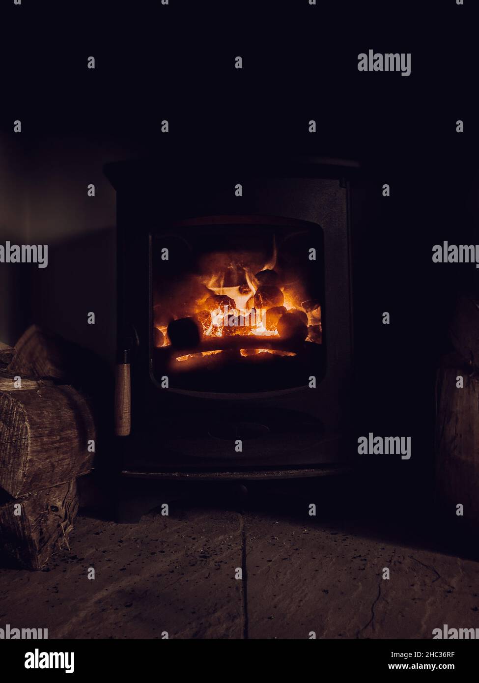 A log and coal multi-fuel burner with orange fire flames flickering in a countryside cottage. Carbon emissions from log fireplaces are high in the UK. Stock Photo