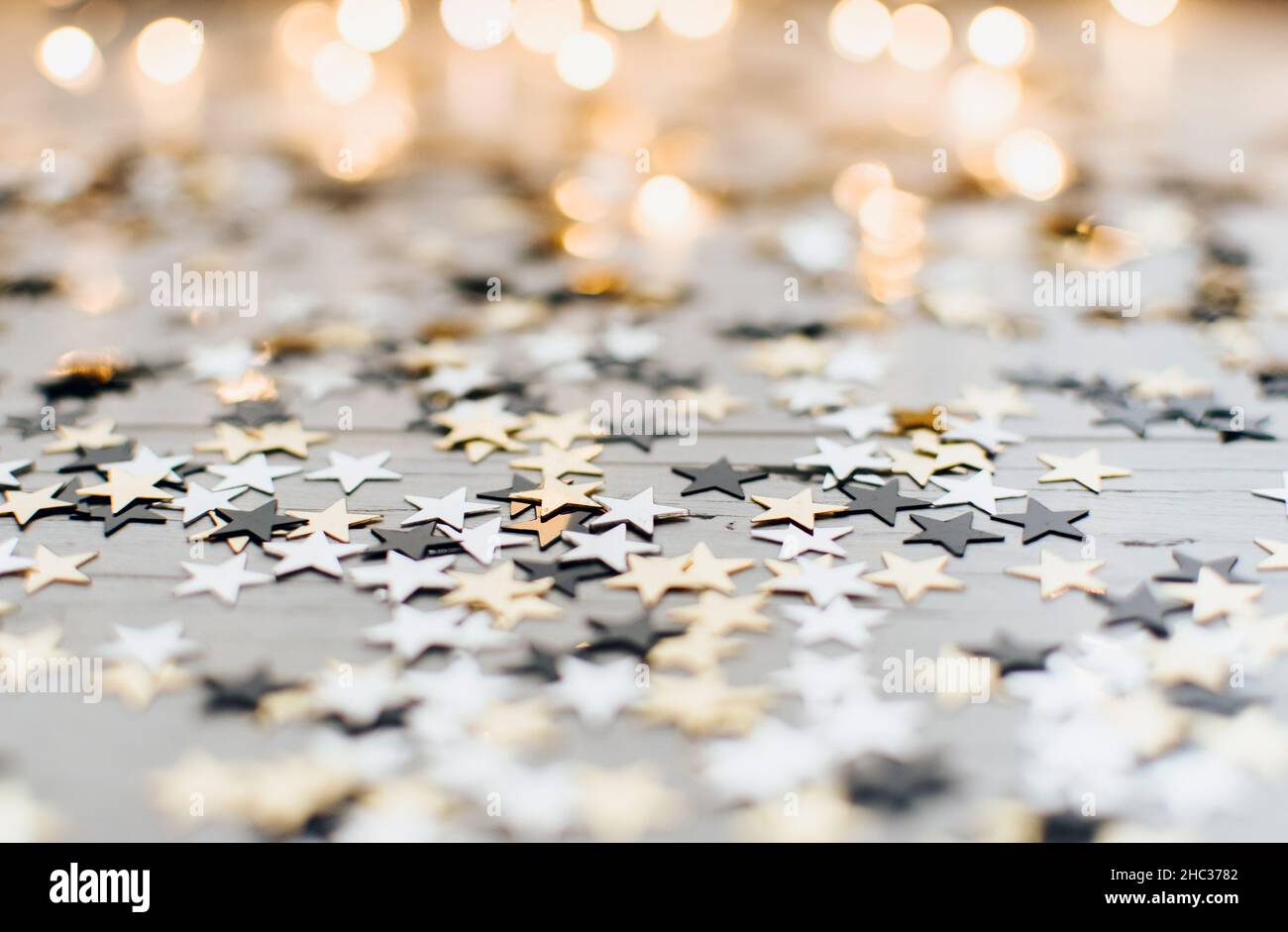 Star shaped new year confetti on white surface in front of bokeh lights Stock Photo