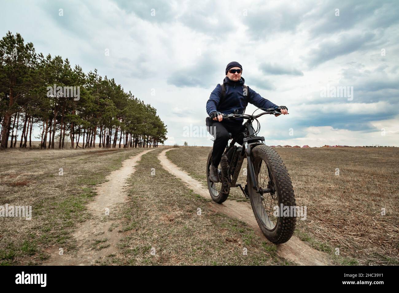 A man rides through the countryside on an electric bike with thick wheels. Sports hobby. Stock Photo