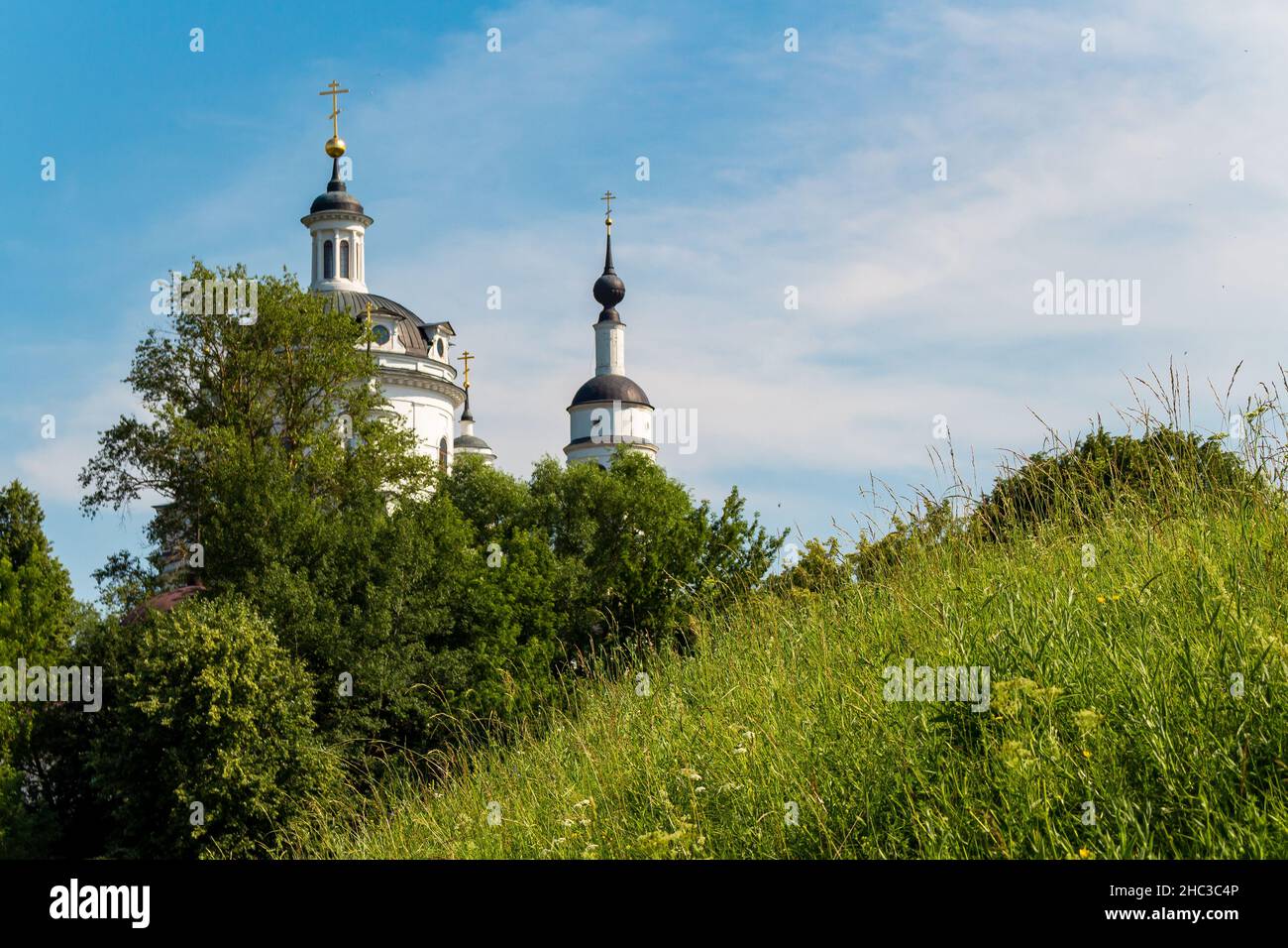 View of the Russian Orthodox Cathedral behind a hill overgrown with green grass. Maloyaroslavets, Russia Stock Photo