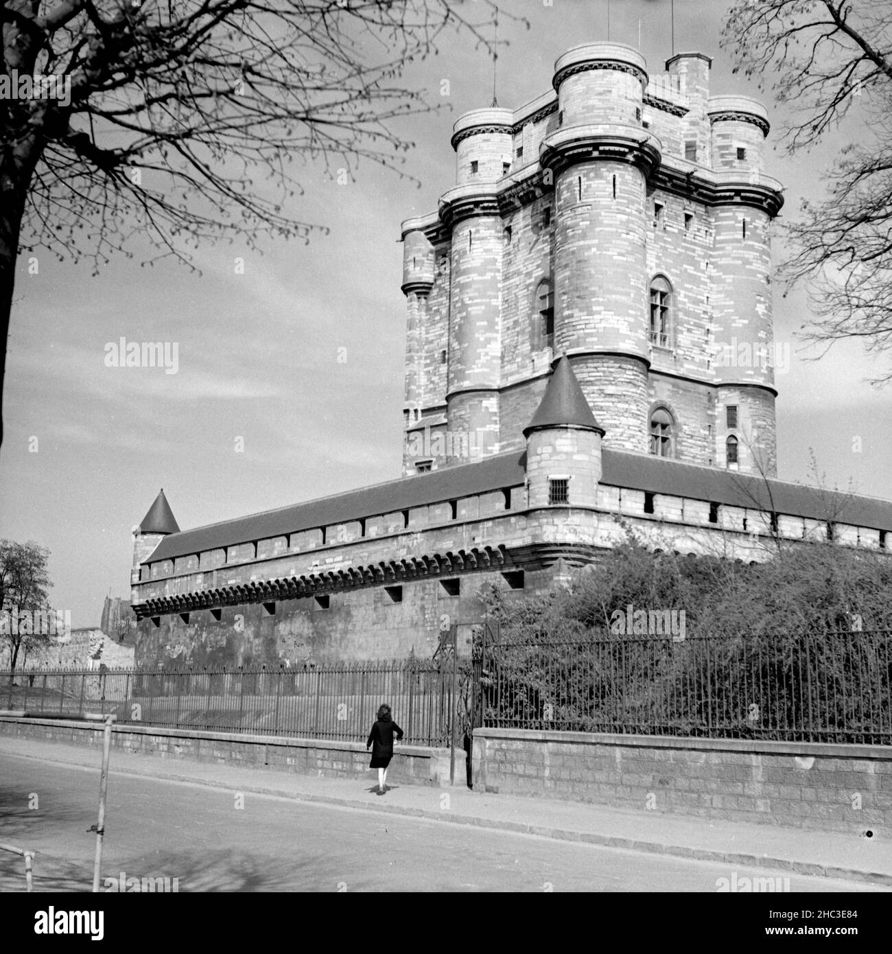 Paris Château de Vincennes, a woman walks outside the fortress walls, 1945. An early 1945 photograph taken from outside the west wall of the fortress shows a woman walking alone along the western perimeter. The Keep or Donjon rise dramatically above the wall. Ahead of her direction of travel, the edge of the image indicates a break in the fortress wall. Seven months before this photograph was taken, retreating German occupation forces exploded munitions that they stored inside. Stock Photo