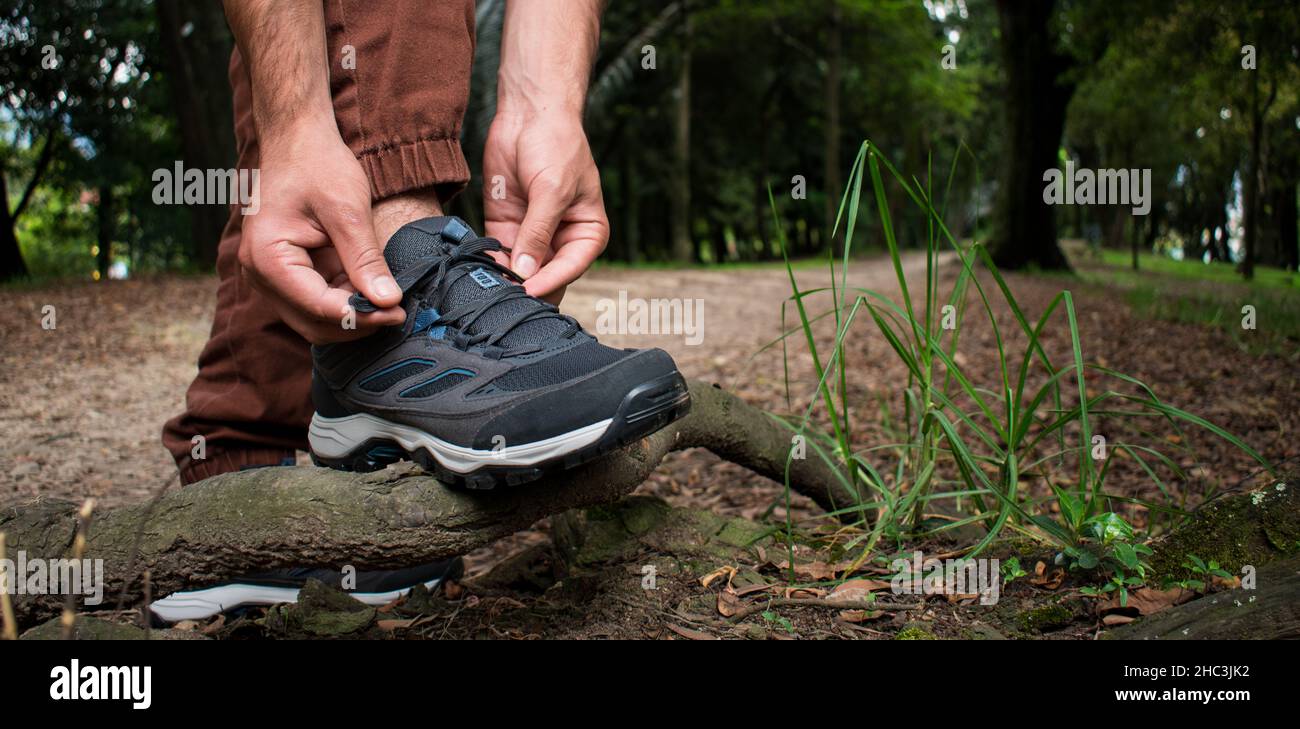 Man tying his trekking shoes on a branch in the middle of a forest for continue walking Stock Photo