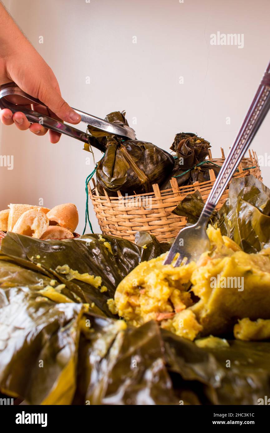 Hand taking a traditional Colombian food known as 'tamal' wrapped with leaves from a basket on a black table Stock Photo