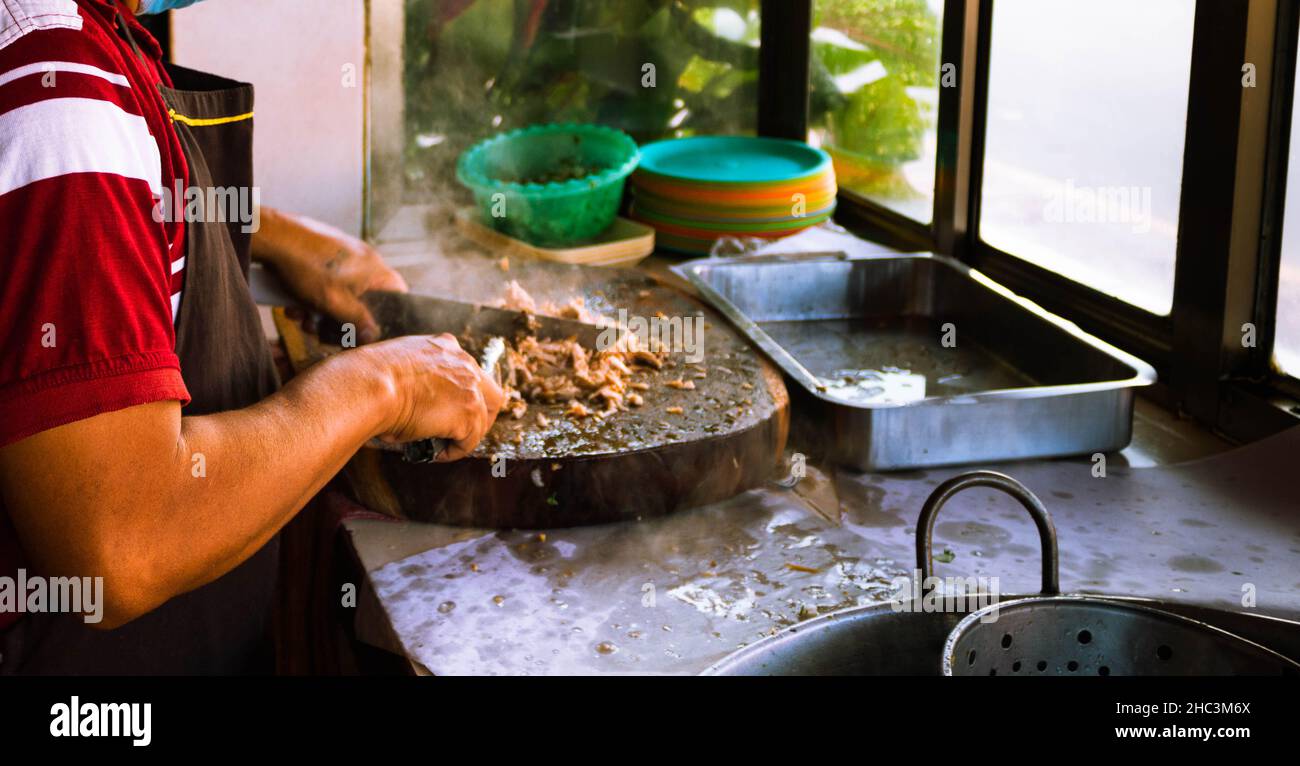 Socumentary photography of a adult male taquero cutting meat at a Mexican restaurant to prepare carnitas tacos. High quality photo Stock Photo