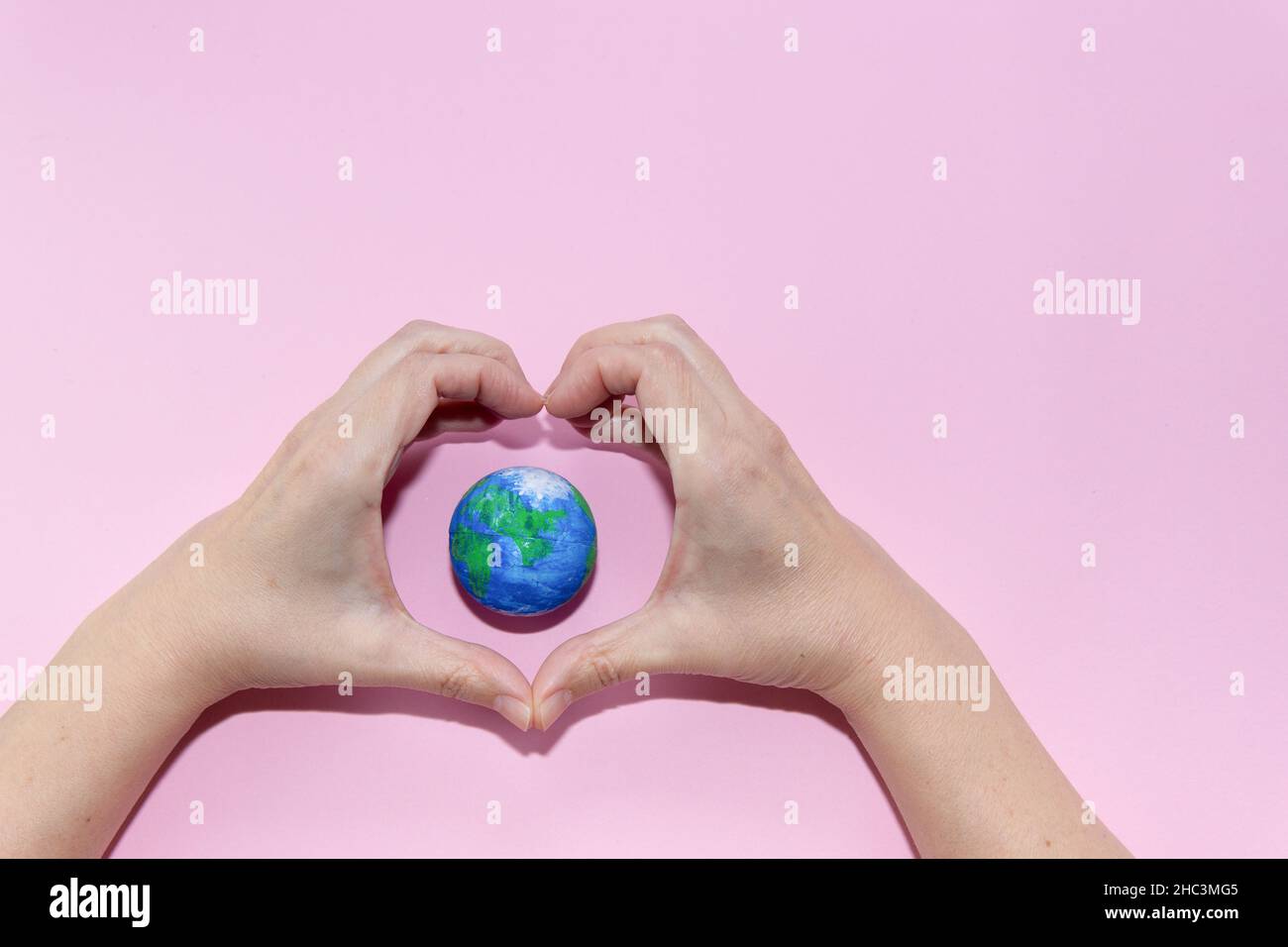 Green Energy, Renewable and Sustainable Resources. Environmental and Ecology Care Concept. Hands doing heart gesture on earth on pastel pink backgroun Stock Photo