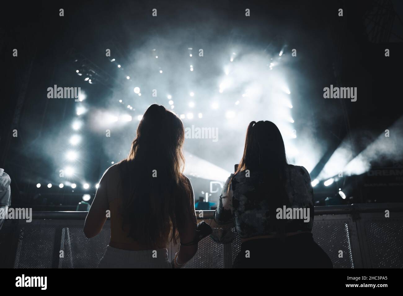 Back view of two women enjoying the concert and taking photos with a phone Stock Photo
