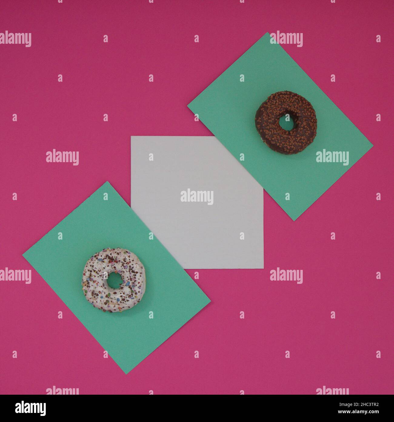 Two donuts sprinkled with chocolate crumbs on a light green surface, with white copy space, all on a pink background. Minimal flat flay composition. Stock Photo