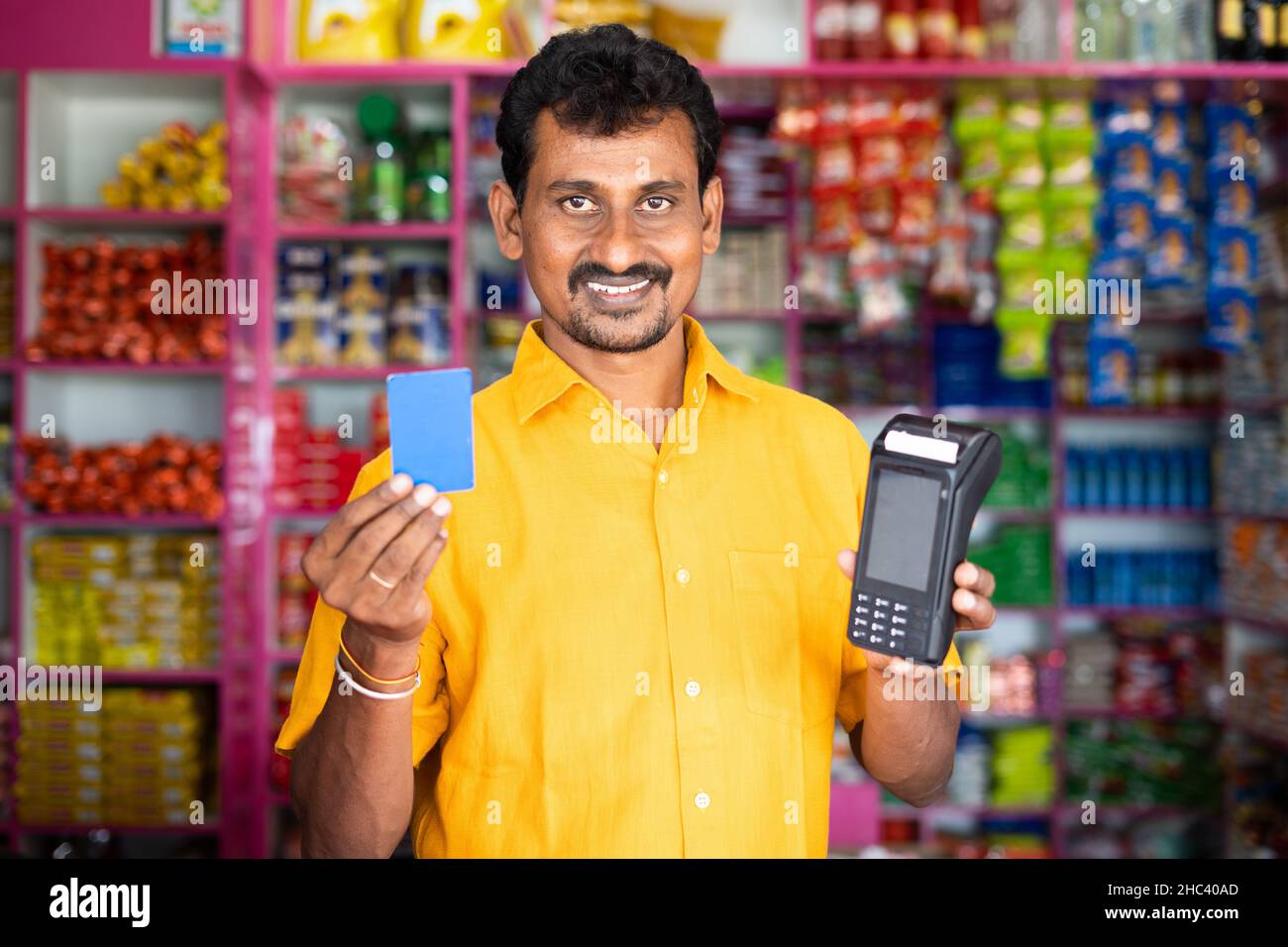 Kirana or groceries merchant showing credit card and swiping POS machine - concept of accepting Digital payment in retail business, cashless purchase Stock Photo