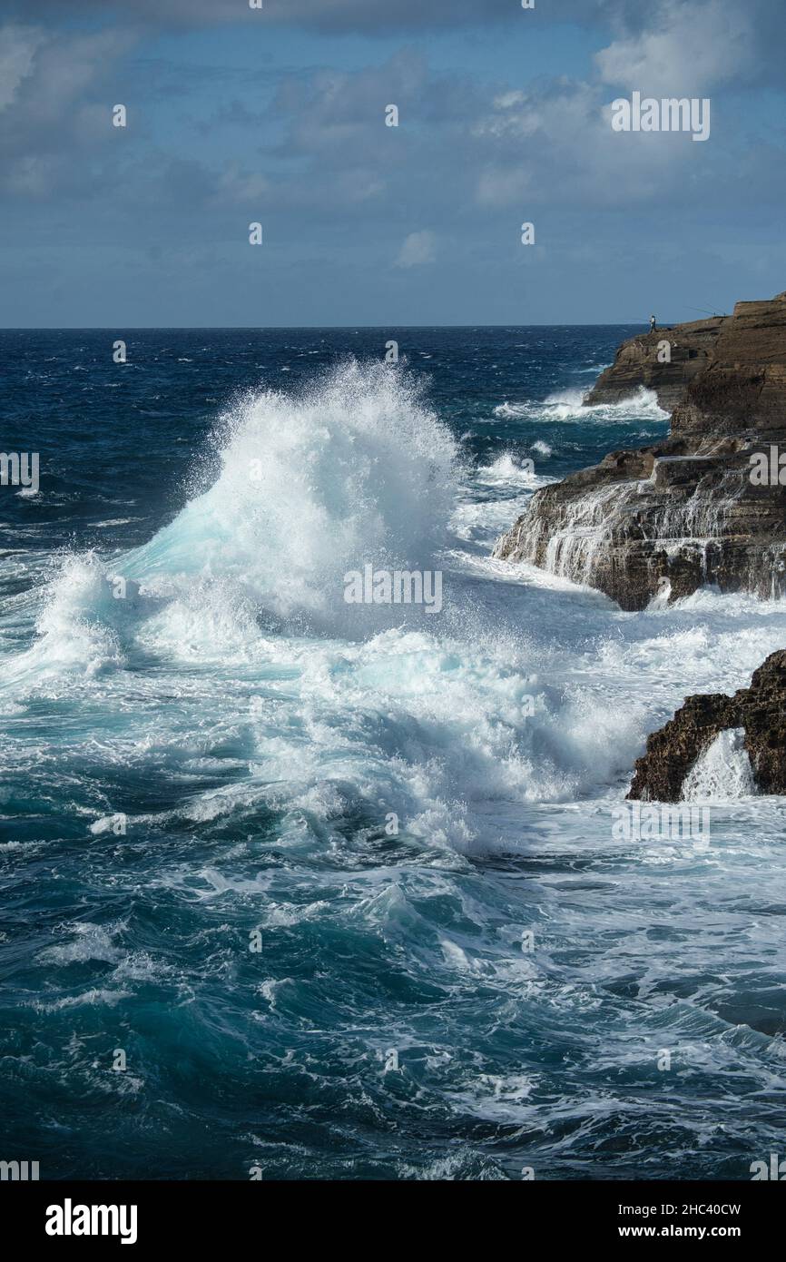 Vertical shot of the blue sea waves splashing against rocks and cliffs ...