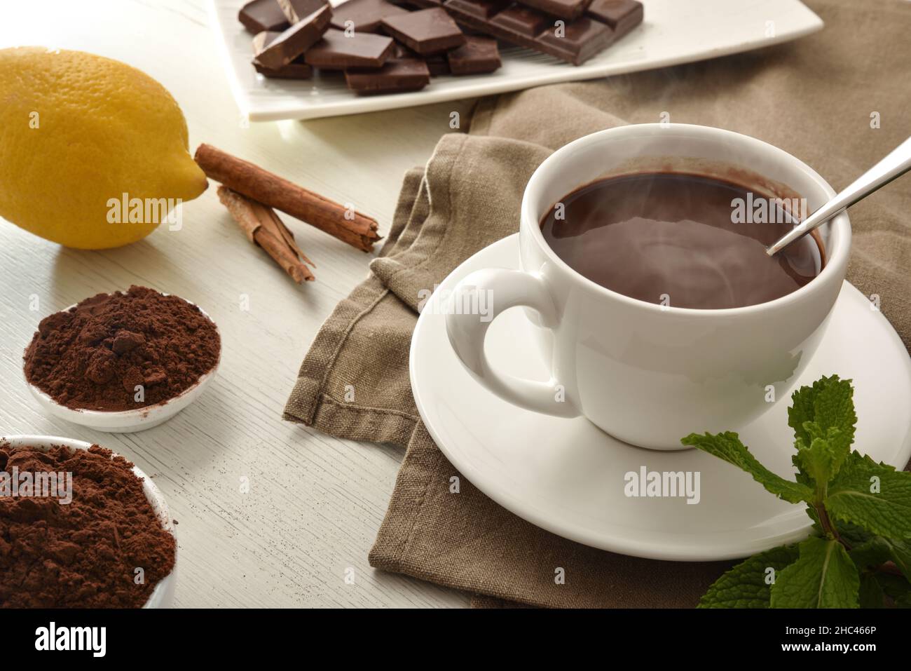Hot chocolate in white ceramic mug, pieces and chocolate powder in bowl on wooden table. Elevated view. Horizontal composition. Stock Photo