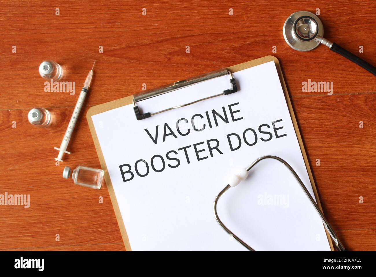 Top view of stethoscope, 3 bottle glass vial, syringe and paper clipboard with text VACCINE BOOSTER DOSE Stock Photo
