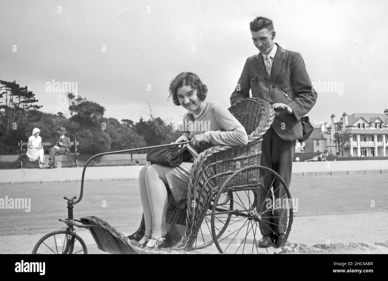 Many pushing woman seated in basket invalid wheelchair on seafront, Isle of Wight 1920s UK Stock Photo