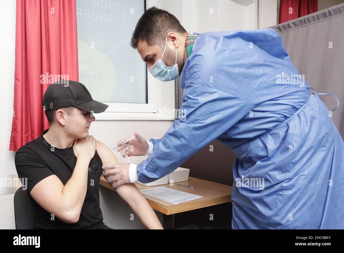 Duisburg, Germany. 24th Dec, 2021. Luke van B. (23, l) is vaccinated  against Corona with the Biontech vaccine by doctor Ahmad-Mujtaba Mostakiem  during a Christmas vaccination marathon in a hotel. Ahmad-Mujtaba Mostakiem