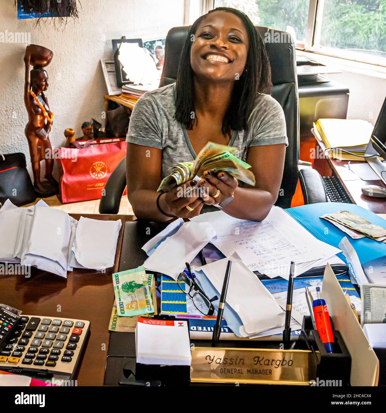A woman counts money at a crowded desk in Hastings, Sierra Leone Stock Photo