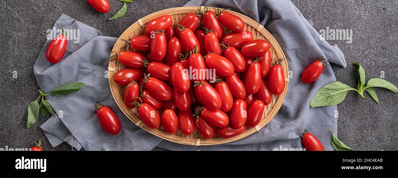 Top view of fresh cherry tomatoes in a basket with basil leaf on gray ...