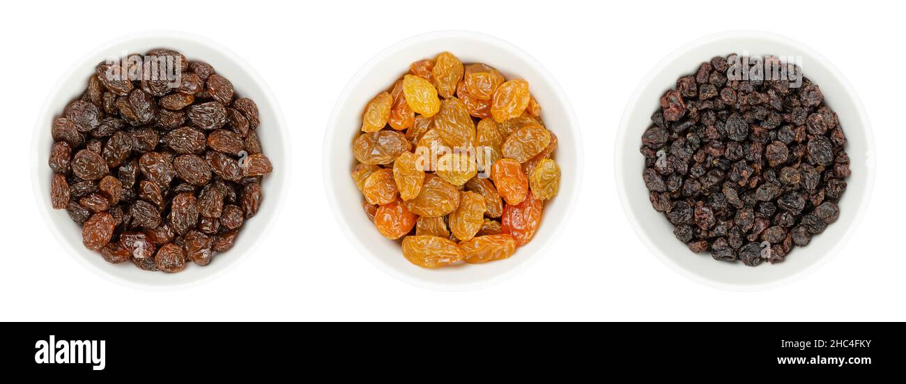 Common commercial raisins, golden raisins (Sultanas), and small currants (Zante currants or Black Corinth), in white bowls. Dried seedless grapes. Stock Photo