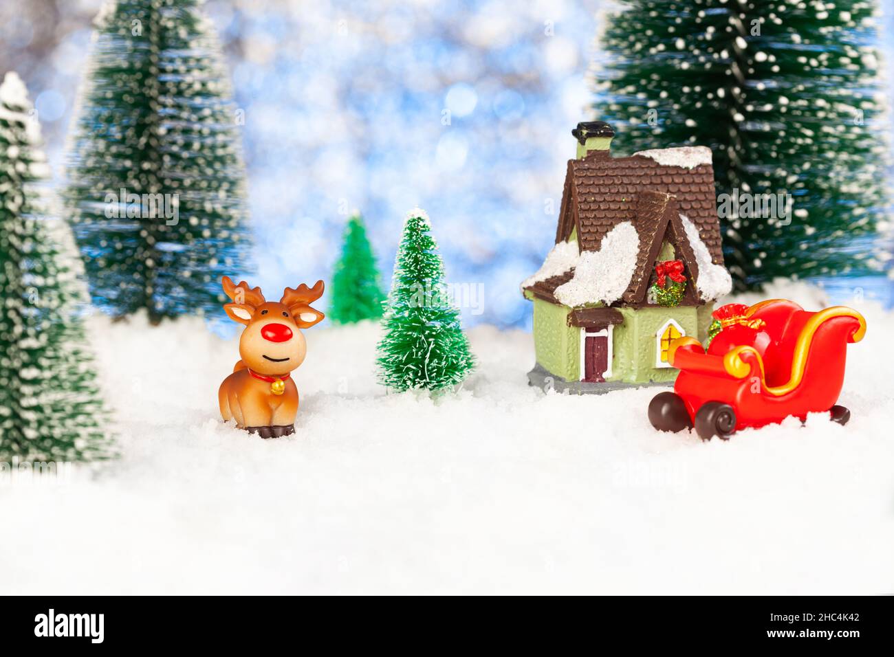 toy sleigh and toy reindeer in the snow near a small house Stock Photo