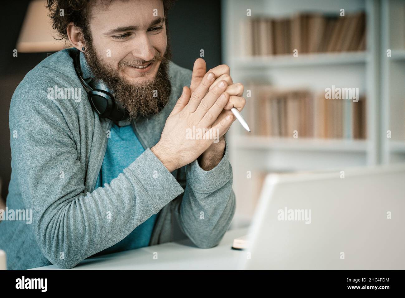 Shy Student Has a Video Lesson Online by his Laptop in his Home Library. Student has Distance Learning During the Quarantine Period. Shelves Full of Books Background. Close-up. High quality photo Stock Photo