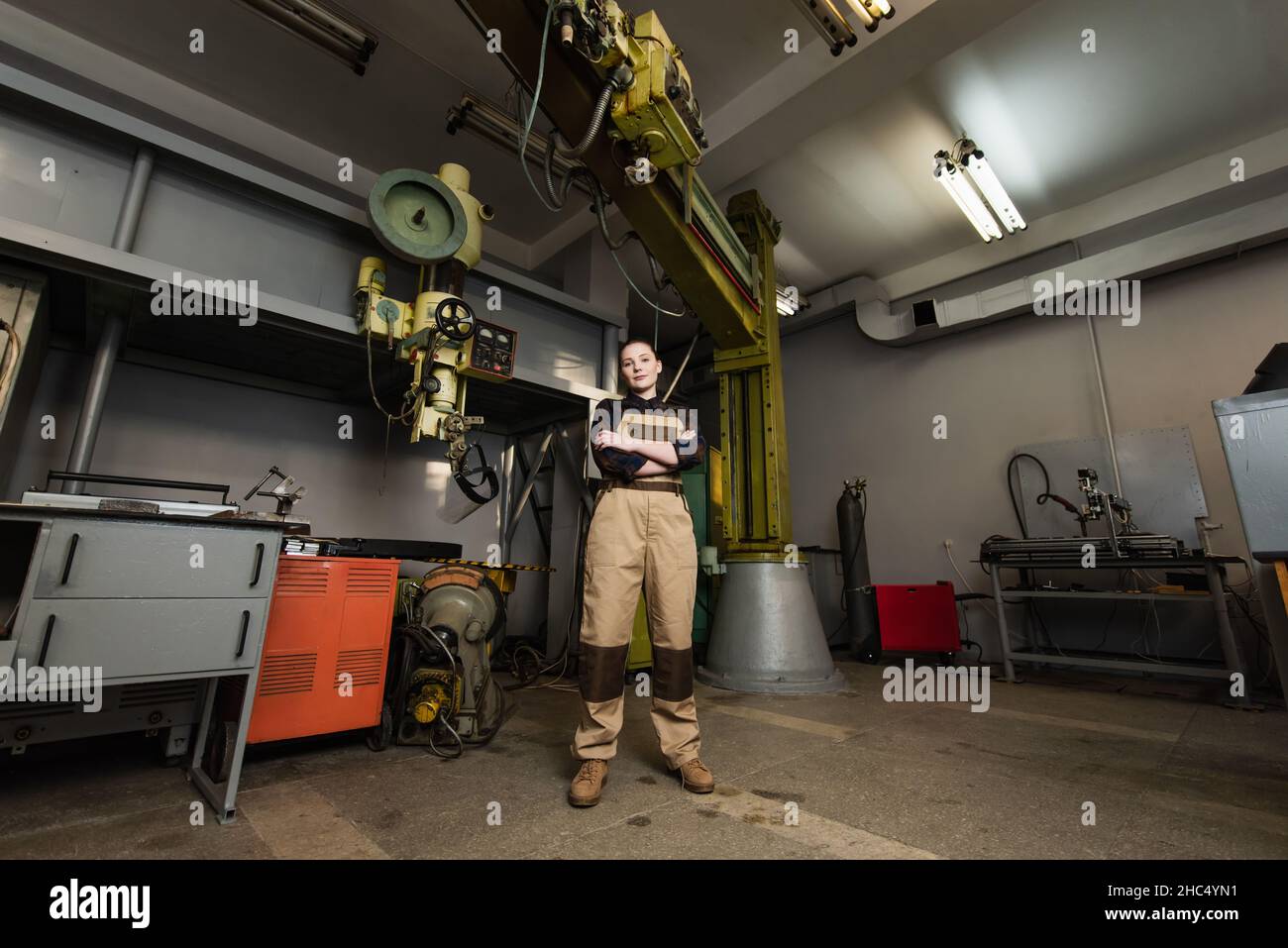 Welder looking at camera near machinery in factory Stock Photo