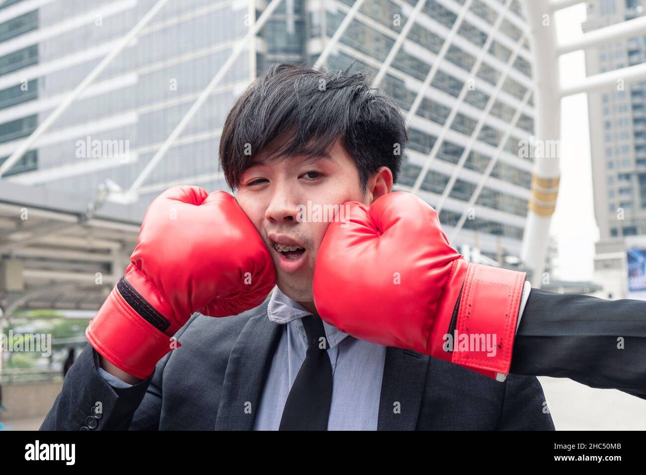 Young asian businessman getting punch with red boxing glove in the city Stock Photo