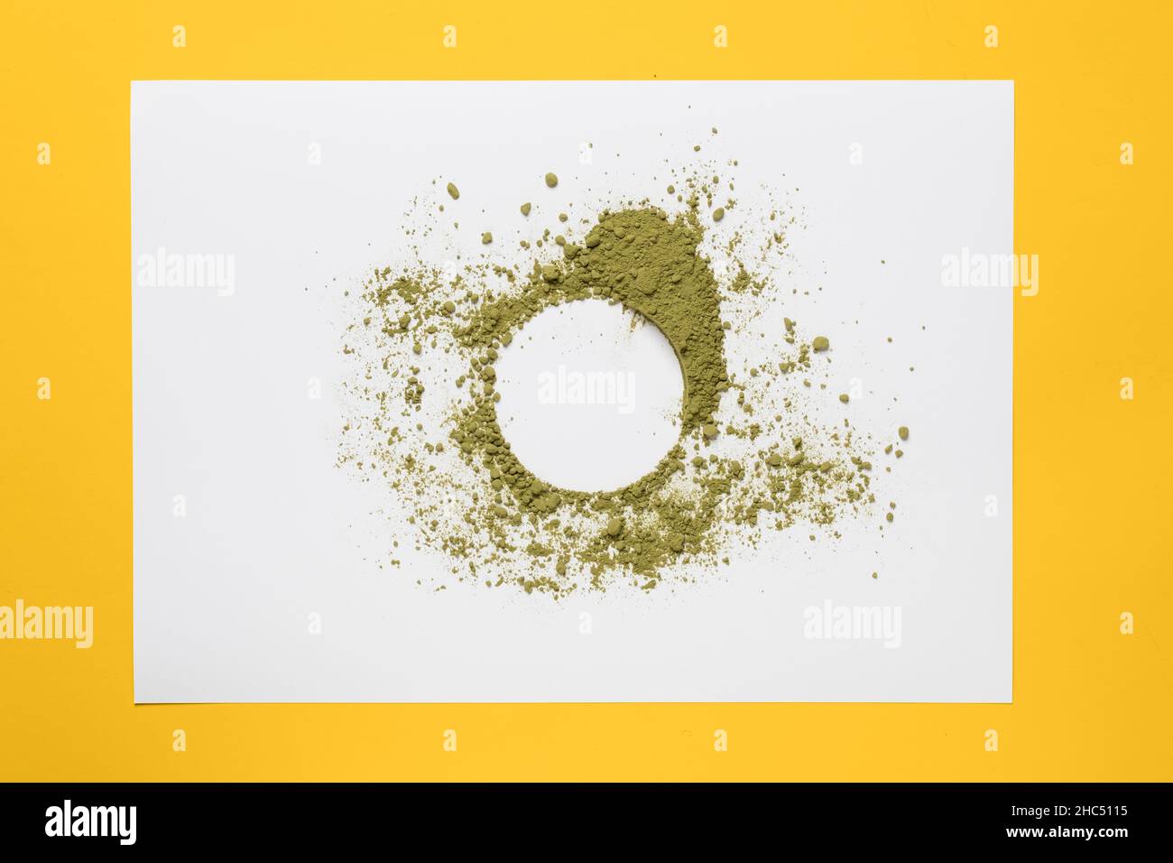 Circle of green powder scattered on a sheet of white paper, on a yellow background. Copy space. Bright dry paint.  Stock Photo