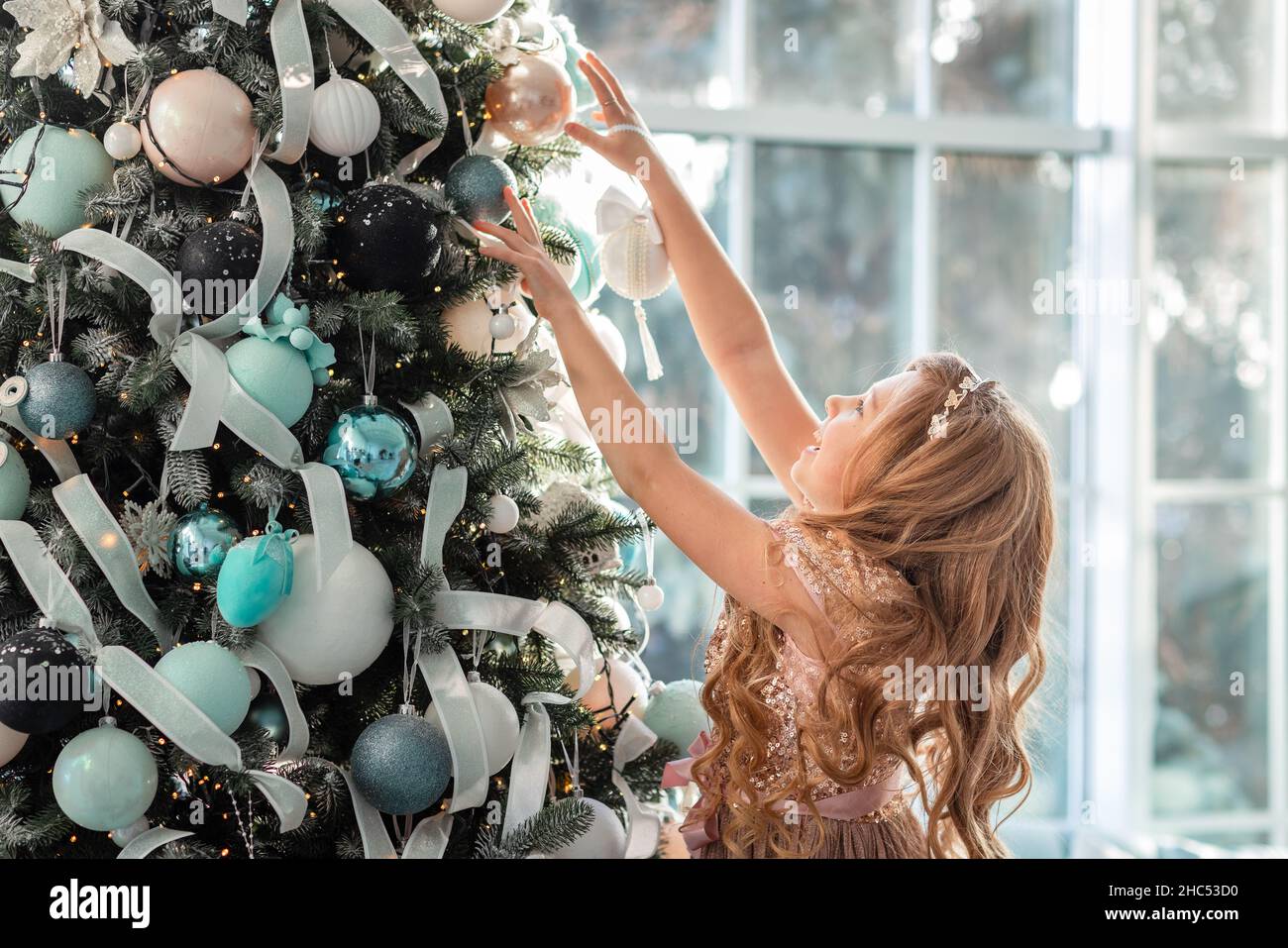 Cute little girl is decorating the Christmas tree indoors. Merry ...