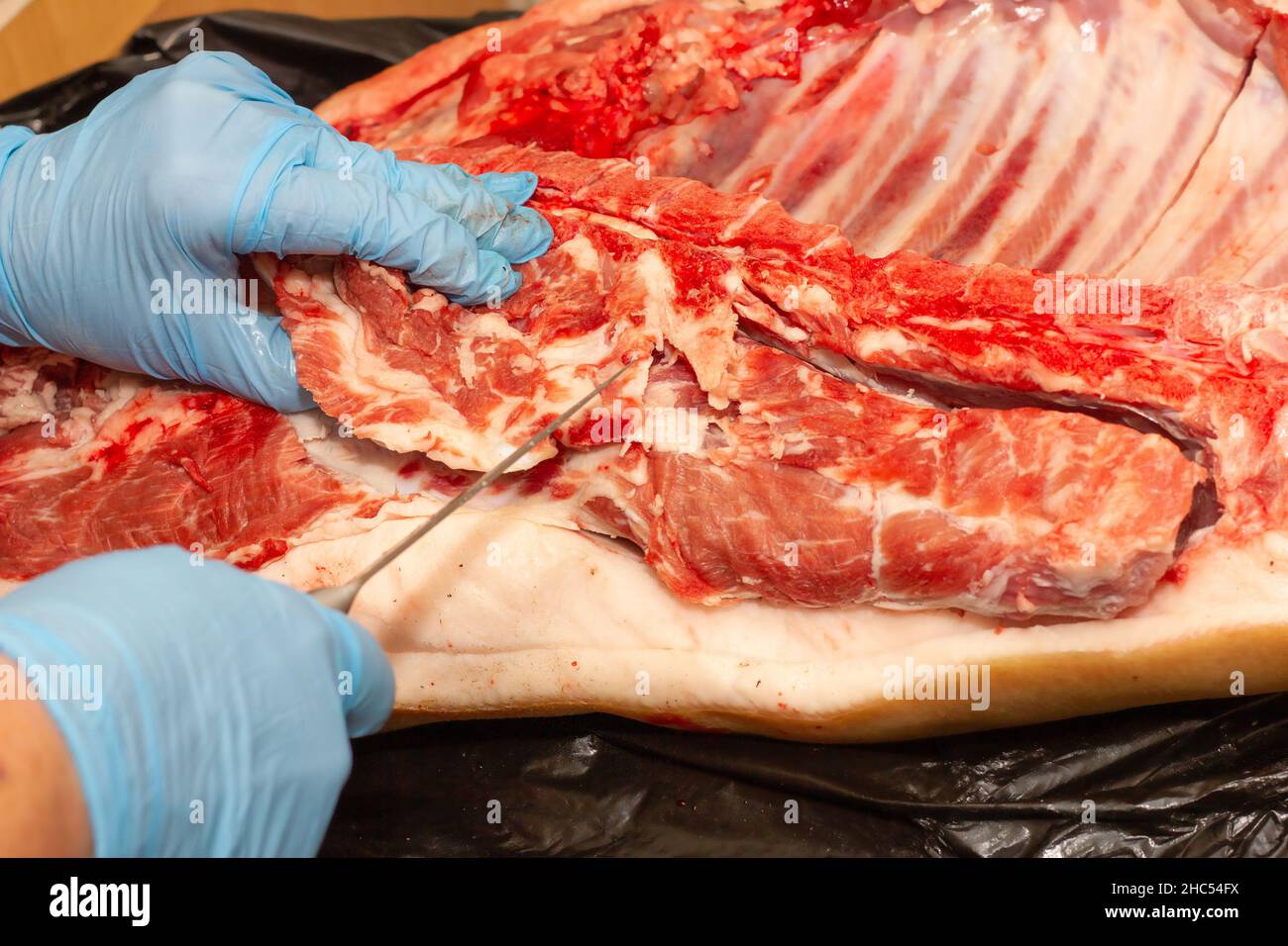 in blue gloves, cut off a piece of meat with a kitchen knife. healthy food concept, diet Stock Photo