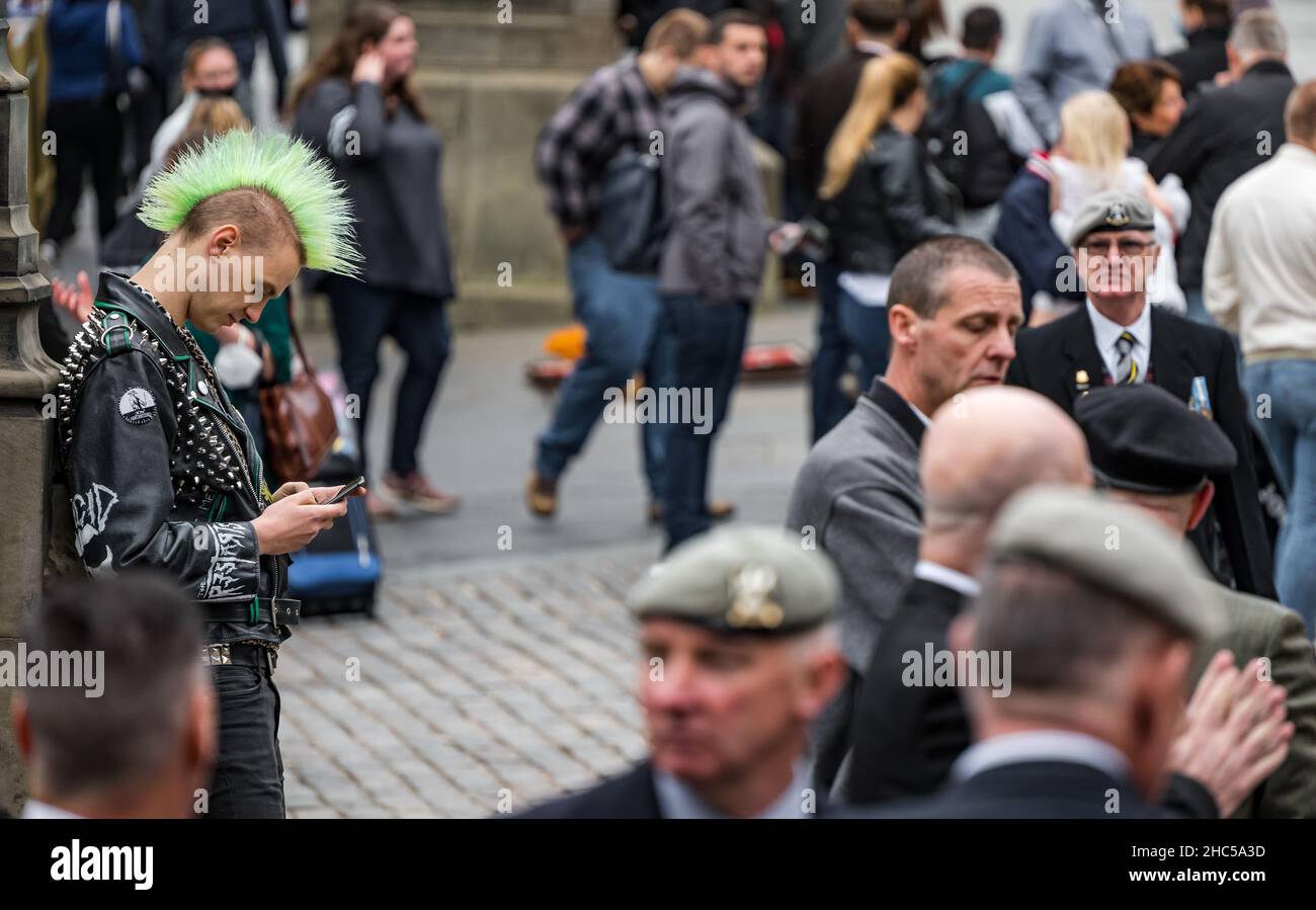 A young man looking at his phone with a punk mohican hair style among a crowd of people, Royal Mile, Edinburgh, Scotland, UK Stock Photo