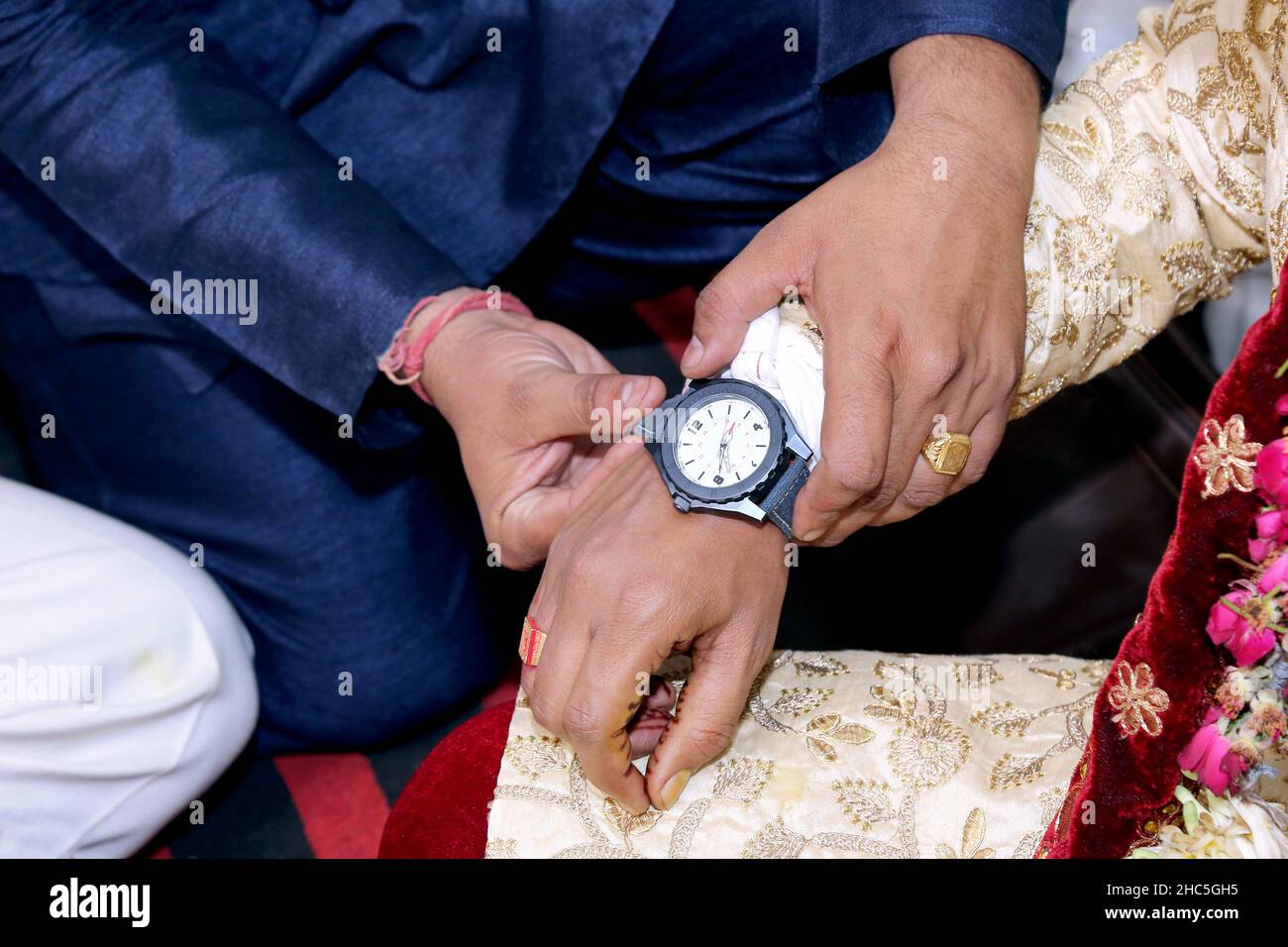 Man in a blue suit putting a watch on a man's hand wearing a traditional suit with flower patterns Stock Photo
