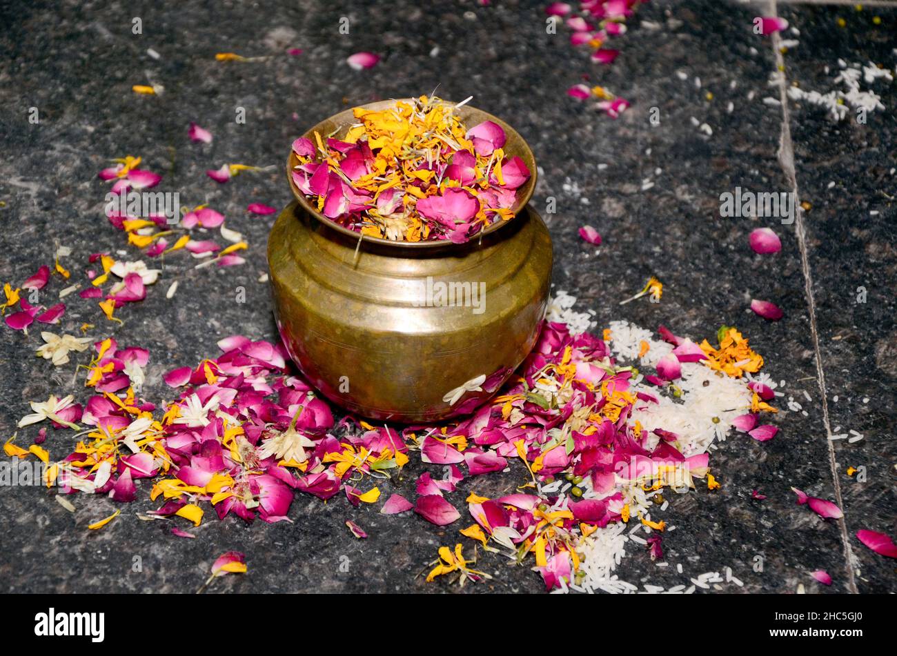 Multicolored flower petals filled in a bronze jar surrounded with petals on the stone background Stock Photo