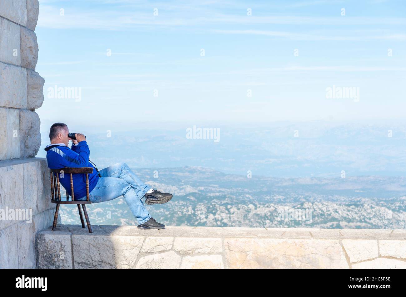 Lovcen,Montenegro-September 14 2019: On the summit of Mount Lovcen,on a warm sunny afternoon,a person sits on a wall in his chair,looking down at the Stock Photo
