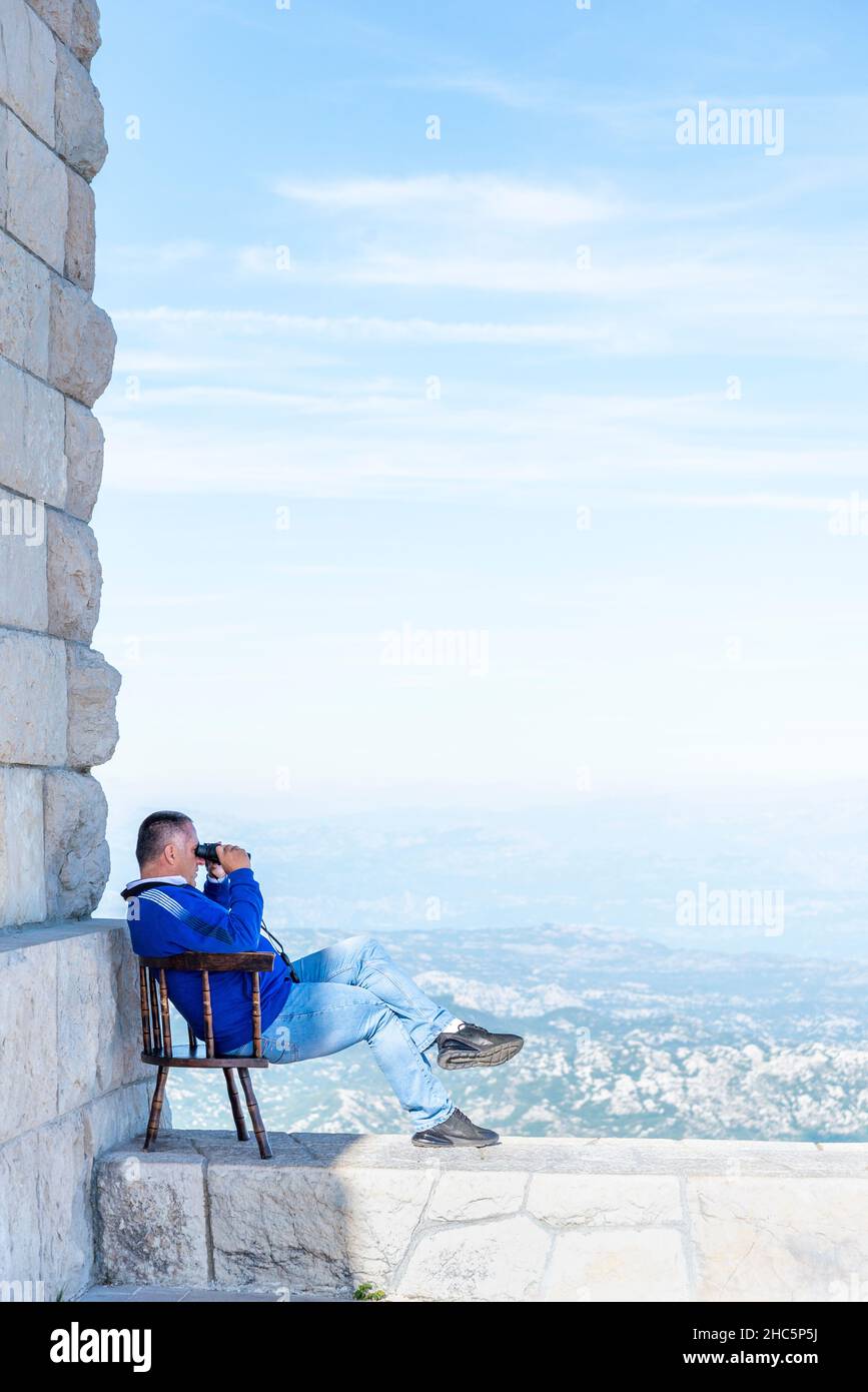 Lovcen,Montenegro-September 14 2019: On the summit of Mount Lovcen,on a warm sunny afternoon,a person sits on a wall in his chair,looking down at the Stock Photo