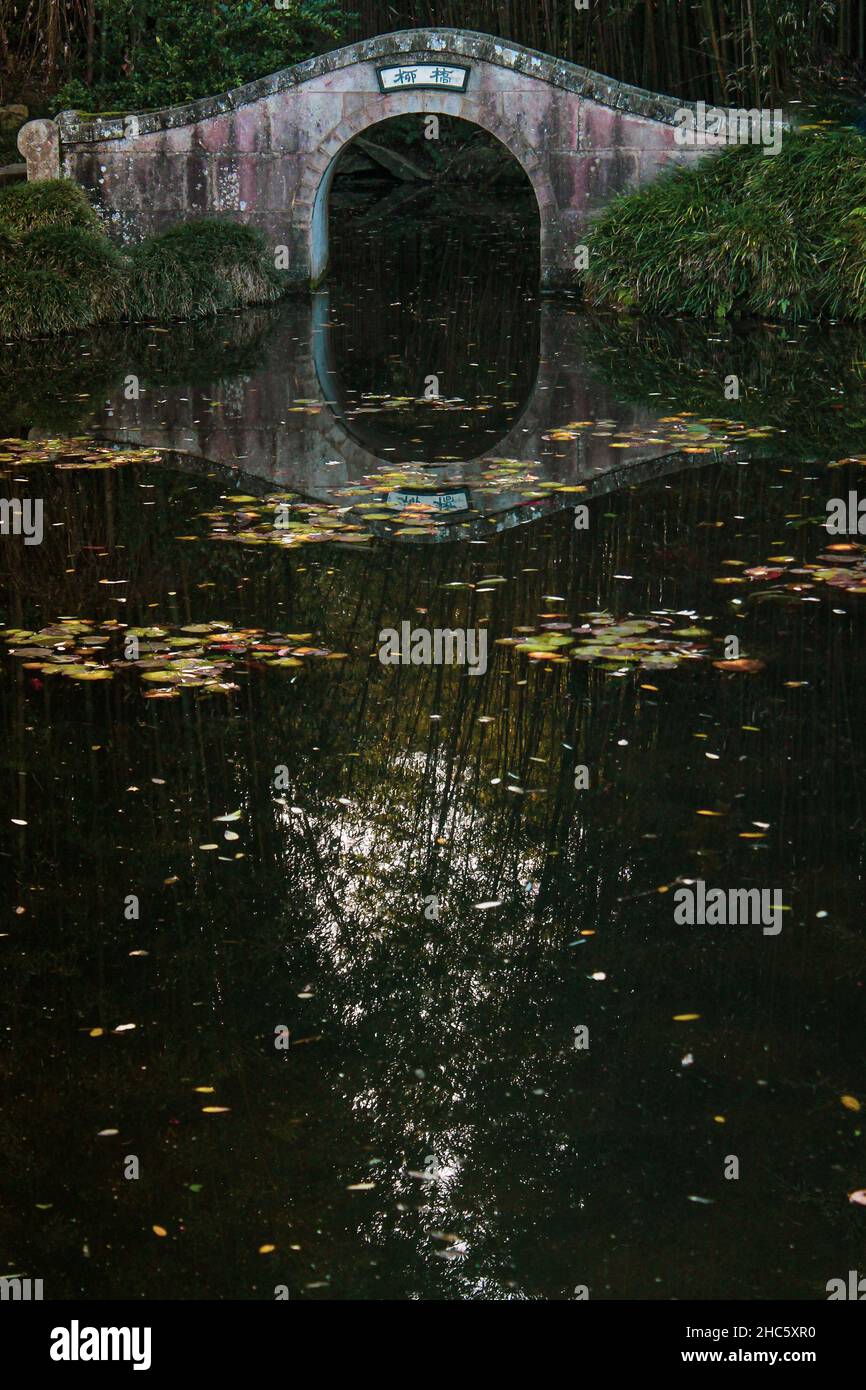 Vertical shot of a stone bridge and reflection of the trees in the river in the autumn Stock Photo